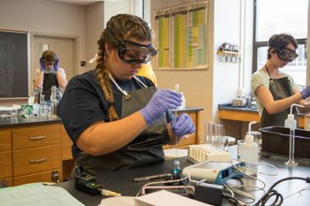 A student wears safety equipment to perform a chemistry lab experiment
