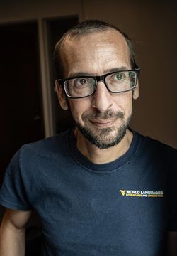 Man with dark rimmed, rectangle glasses and a beard wearing a blue WVU shirt