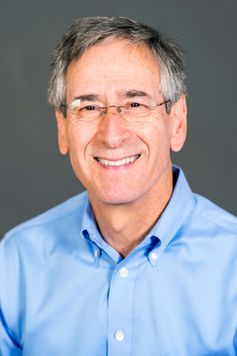 Male with greying hair and rimless glasses wears a button down shirt.