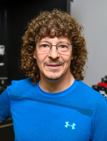 Male with long curly brown hair and glasses wears a long-sleeve Underarmor shirt.