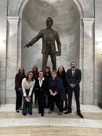 Students pose in front of statue at the WV state capitol
