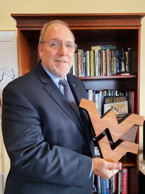 Dean Dunaway holds a wooden flying WV in front of a bookcase