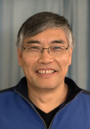 Asian male with short greying hair and wire rim glasses wears a zip up sports shirt
