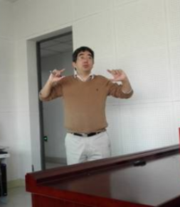 Asian male with dark hair gestures with both hands while teaching. 