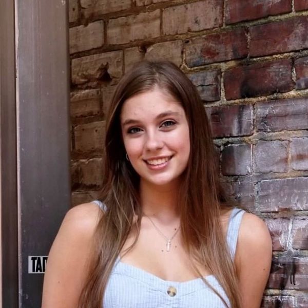 Headshot of WVU student Madyson Kimble. She is pictured leaning against a brick wall. She is wearing a white, button up blouse and her long brown hair is cascading down the front of her. 