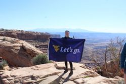 Anastasia Stewart holding "Let's Go" flag on a mountain peak