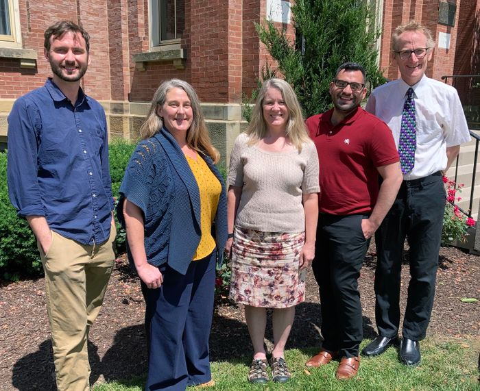 Five staff members standing outside Woodburn Hall on a sunny day