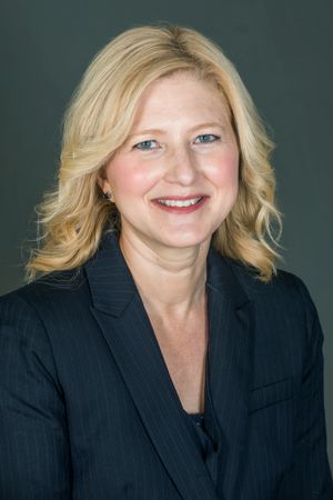 Female with medium length wavy blonde hair wearing a suit jacket.